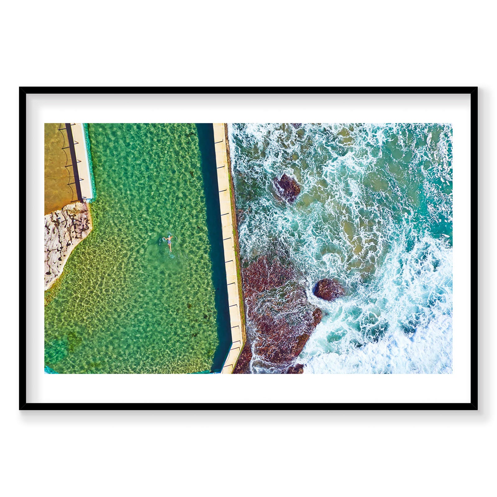 Aerial view of swimmer in emerald pool beside rocky coastline and crashing waves, photography print by Remy Gerega