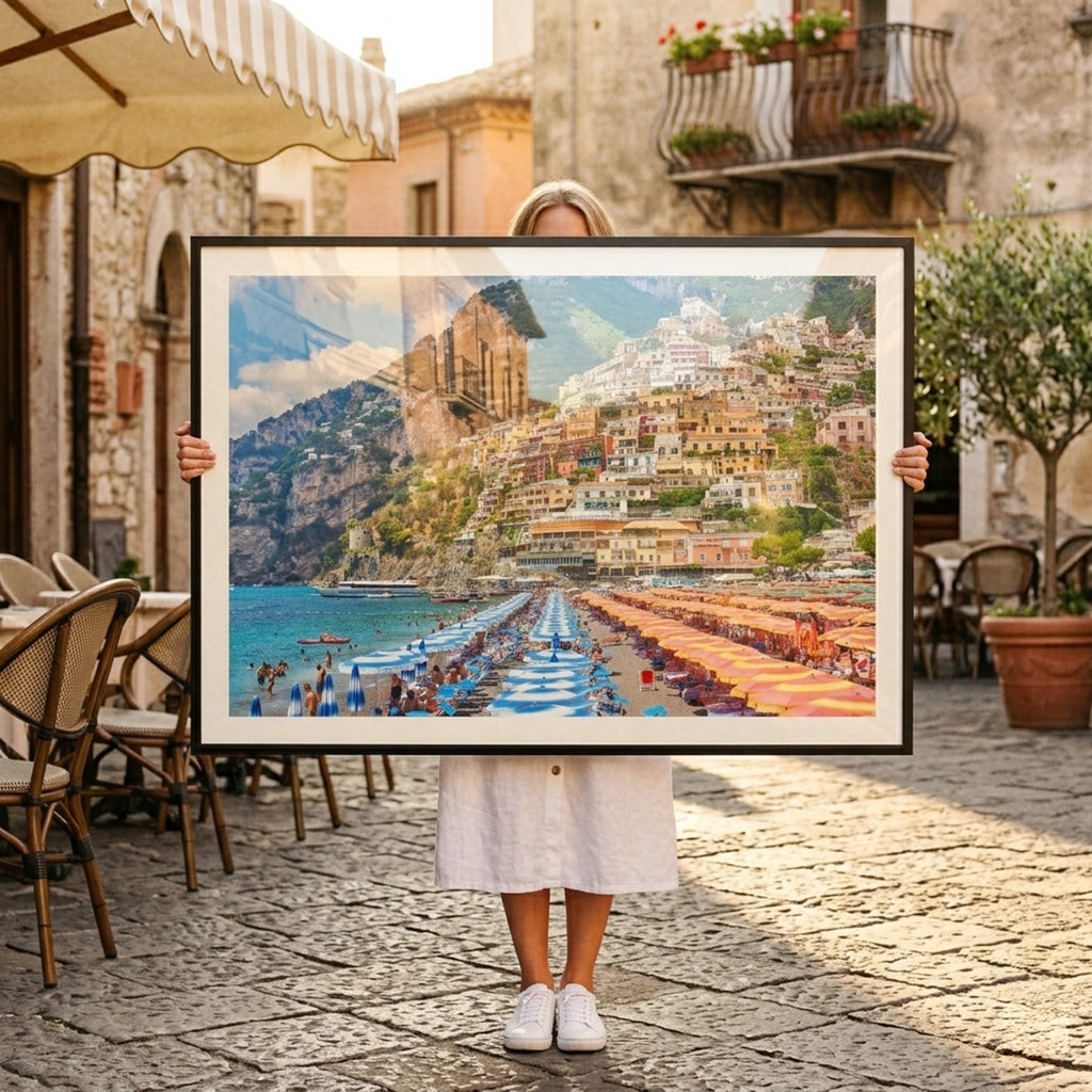 Person holding a framed photograph of a Positano, Italy with mountains in an outdoor setting.