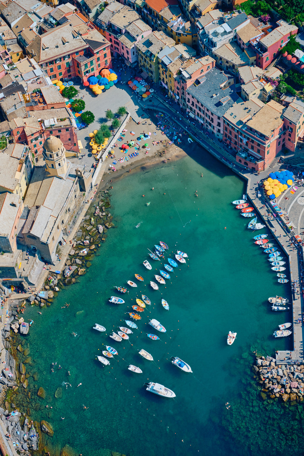 Overhead view of colourful waterfront buildings, a small beach, boats and swimmers in Vernazza harbour, Cinque Terre, Italy, print-only presentation.