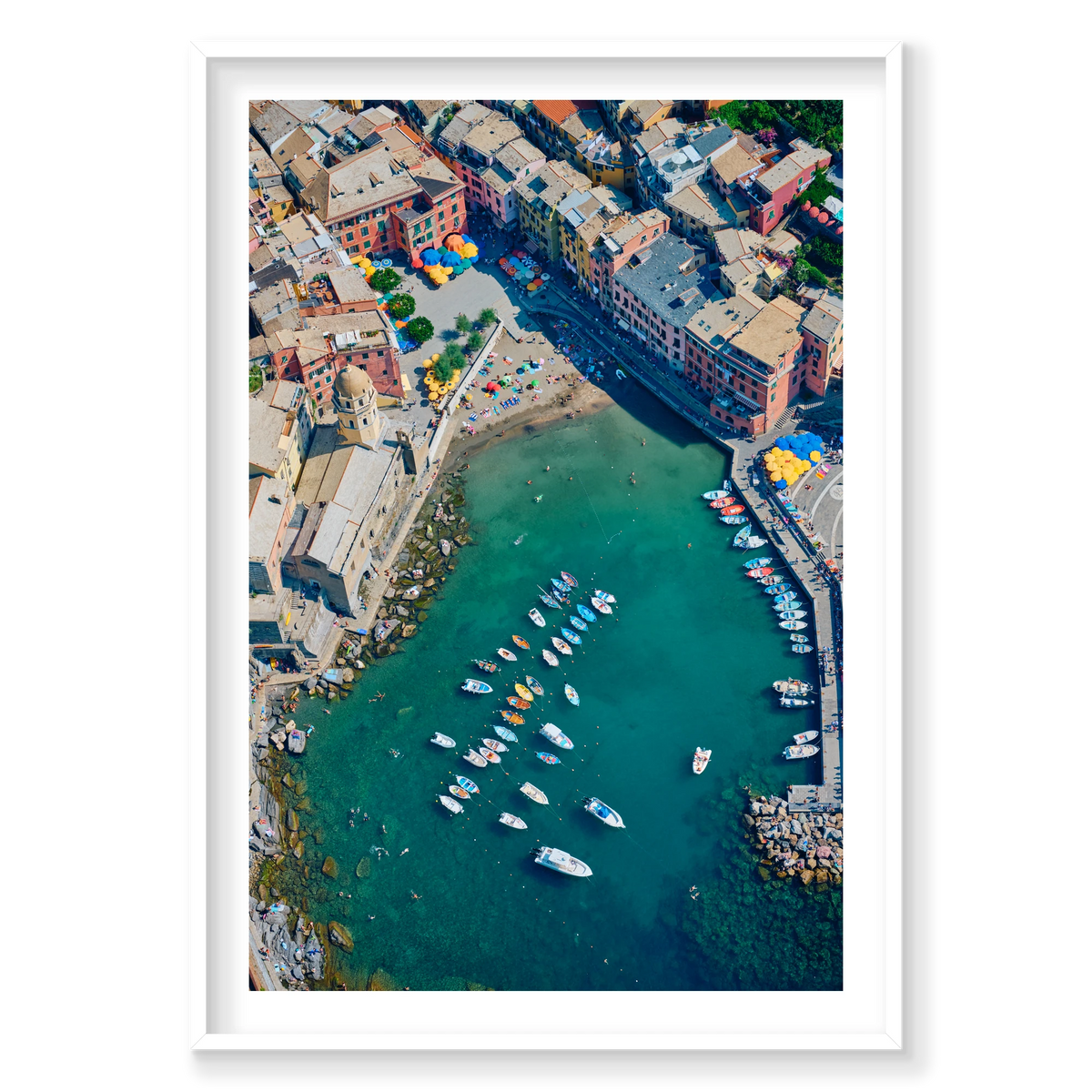 Overhead view of colourful waterfront buildings, a small beach, boats and swimmers in Vernazza harbour, Cinque Terre, Italy, white frame.