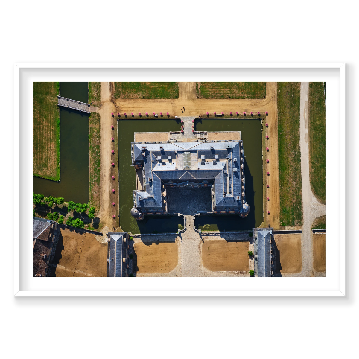 Overhead view of a French château surrounded by a green moat, pale paths, bridges and pink flowers in the Paris region; white frame