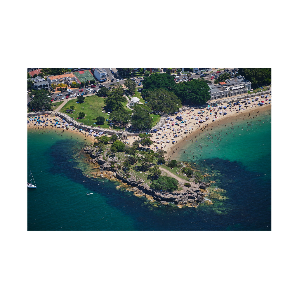 Balmoral Beach in Sydney from above, with swimmers in green water, beach shelters and a rocky point.