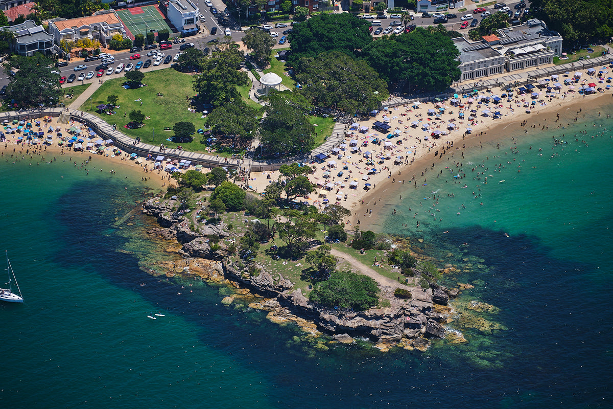 Balmoral Beach in Sydney from above, with swimmers in green water, beach shelters and a rocky point.