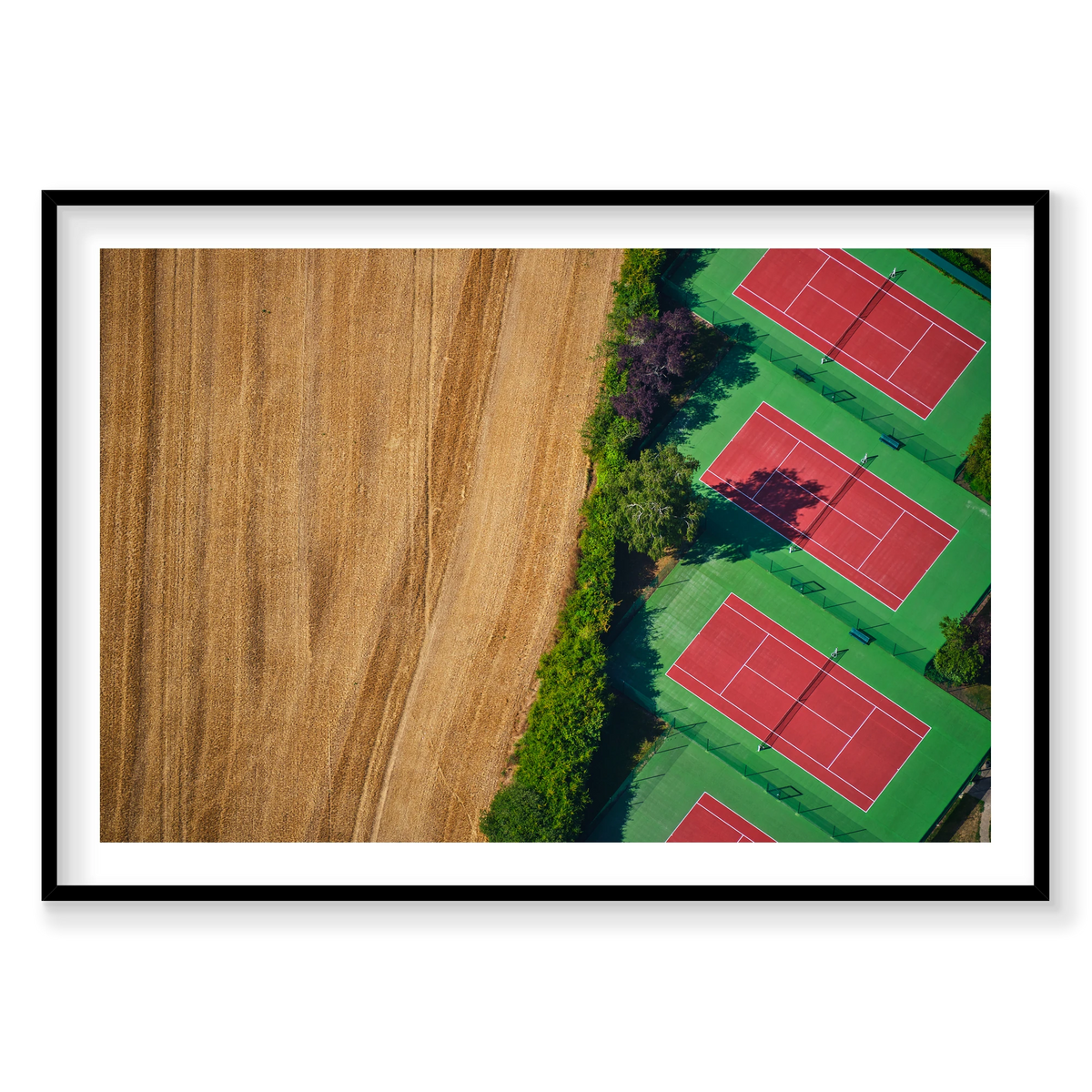 Red tennis courts with green surrounds beside a golden field, seen from above in the Paris region, France; black frame