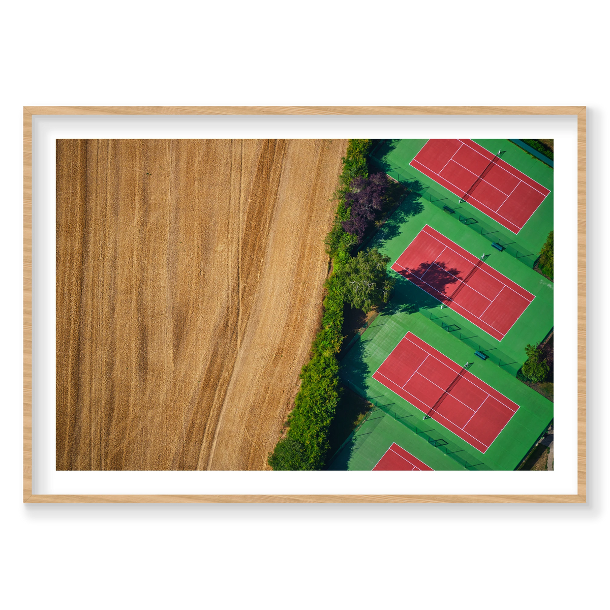 Red tennis courts with green surrounds beside a golden field, seen from above in the Paris region, France; natural timber frame