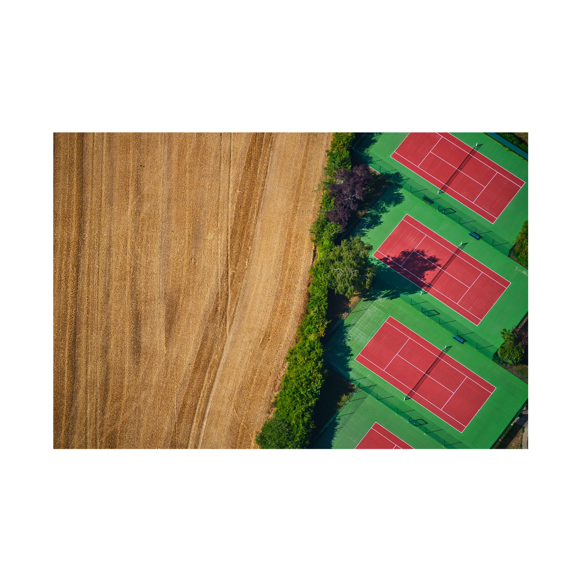 Red tennis courts with green surrounds beside a golden field, seen from above in the Paris region, France; print only