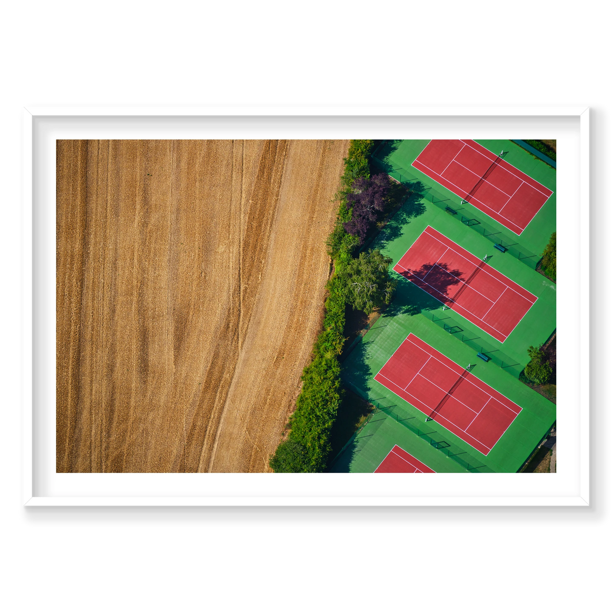 Red tennis courts with green surrounds beside a golden field, seen from above in the Paris region, France; white frame