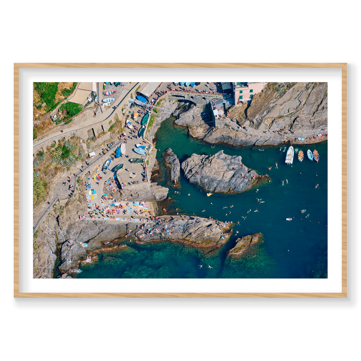 Overhead view of swimmers, boats and sunbathers around Manarola’s rocky harbour, Cinque Terre, Italy, natural timber frame.