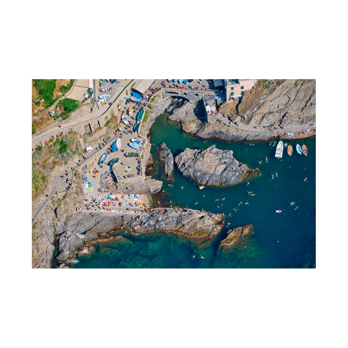 Overhead view of swimmers, boats and sunbathers around Manarola’s rocky harbour, Cinque Terre, Italy, print-only presentation.