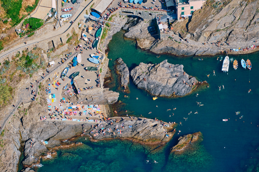 Overhead view of swimmers, boats and sunbathers around Manarola’s rocky harbour, Cinque Terre, Italy, print-only presentation.