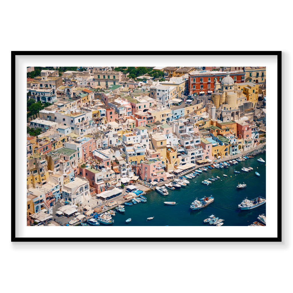 Pastel waterfront buildings, balconies and small boats on deep blue water in Procida, Italy, black frame.