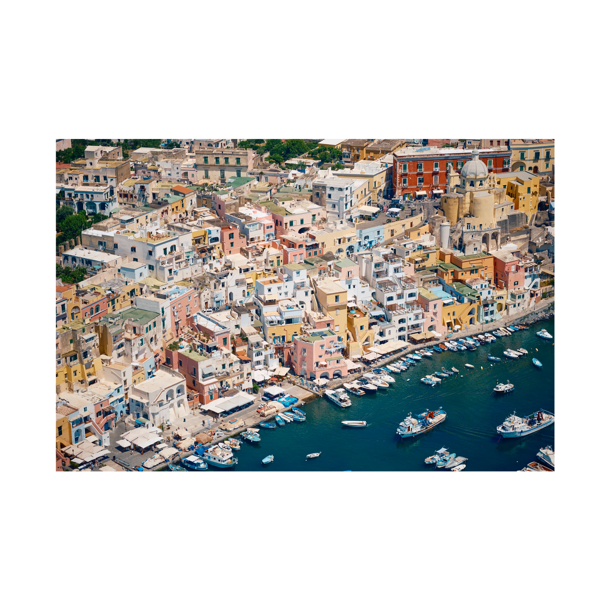 Pastel waterfront buildings, balconies and small boats on deep blue water in Procida, Italy, print-only presentation.