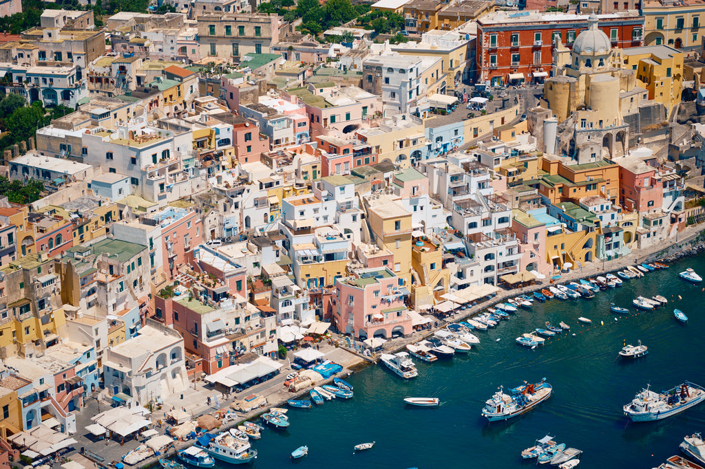 Pastel waterfront buildings, balconies and small boats on deep blue water in Procida, Italy, print-only presentation.