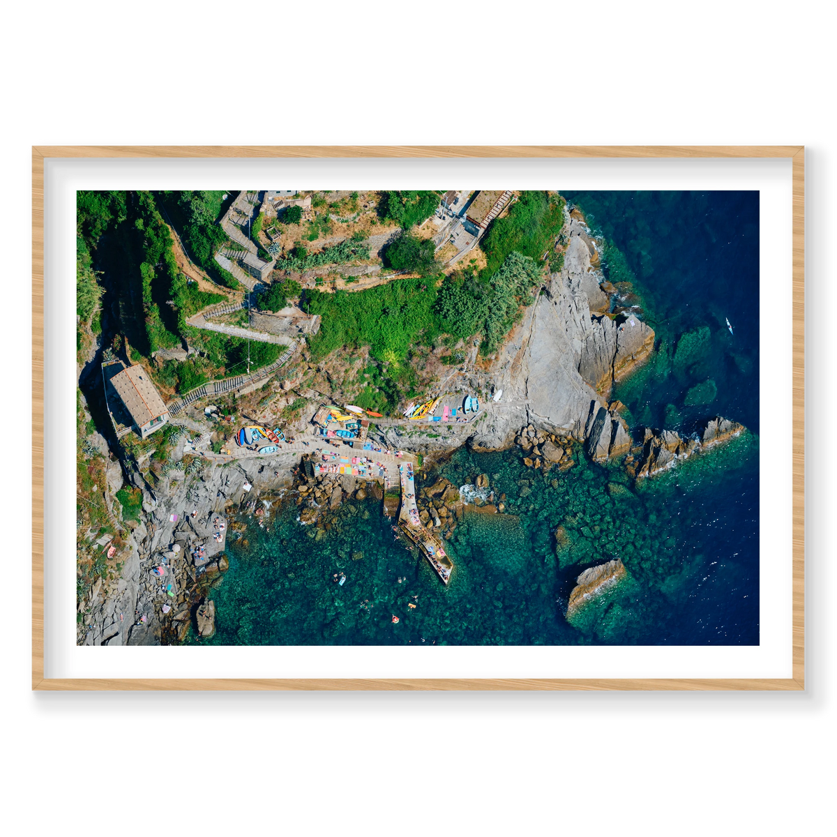 Overhead view of winding hillside steps, colourful boats, a rocky landing and swimmers in clear water at Corniglia, Cinque Terre, Italy, natural timber frame.
