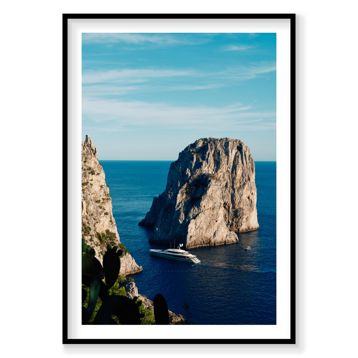 Endeavour 2 yacht beneath the cliffs of Capri, Italy, with blue sea, open sky and cactus in the foreground, black frame.