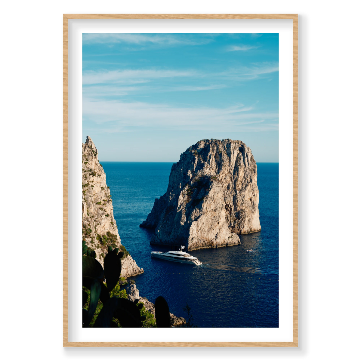 Endeavour 2 yacht beneath the cliffs of Capri, Italy, with blue sea, open sky and cactus in the foreground, natural timber frame.