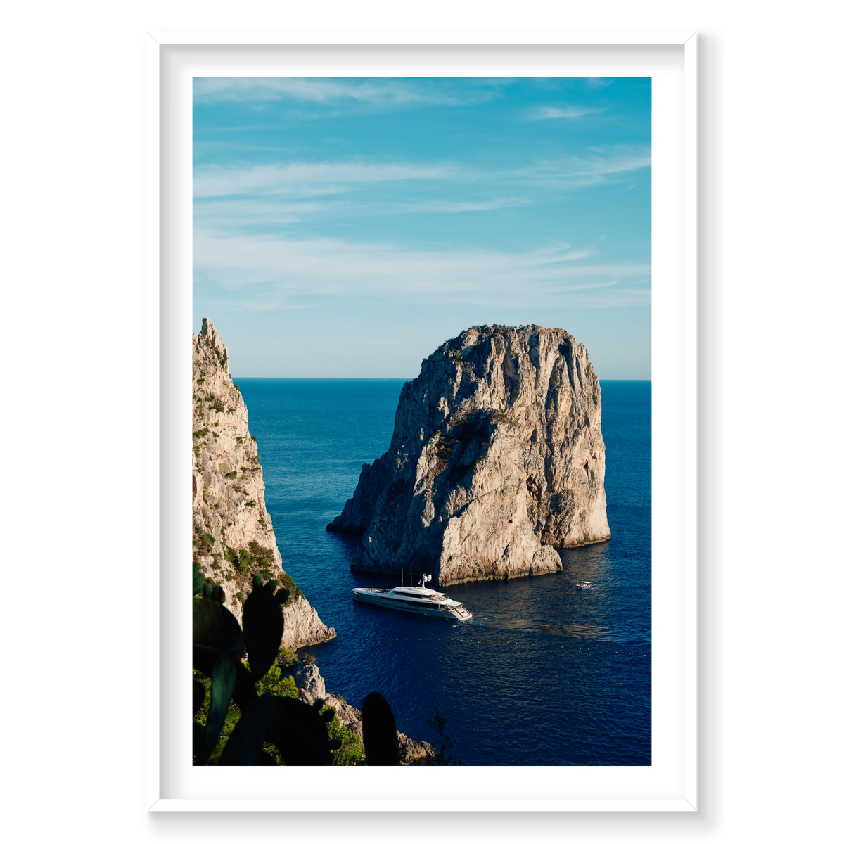 Endeavour 2 yacht beneath the cliffs of Capri, Italy, with blue sea, open sky and cactus in the foreground, white frame.