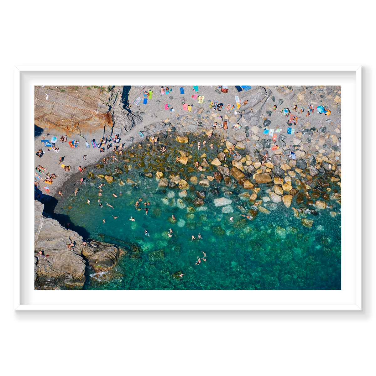 Overhead view of swimmers among boulders in clear green water, with bright towels on a rocky beach at Vernazza, Cinque Terre, Italy, white frame.
