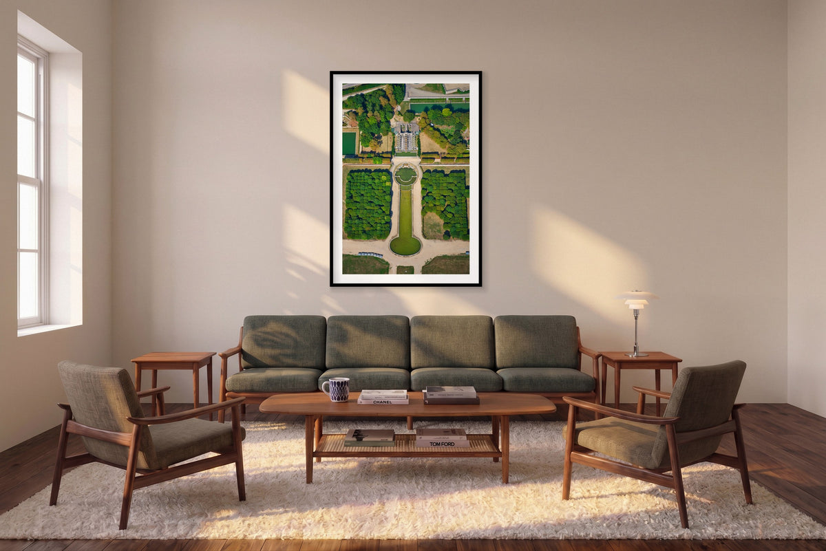 Overhead view of formal gardens in the Paris region, with green pools, pale paths, rows of trees and an ornate cascade; black framed print in a room setting