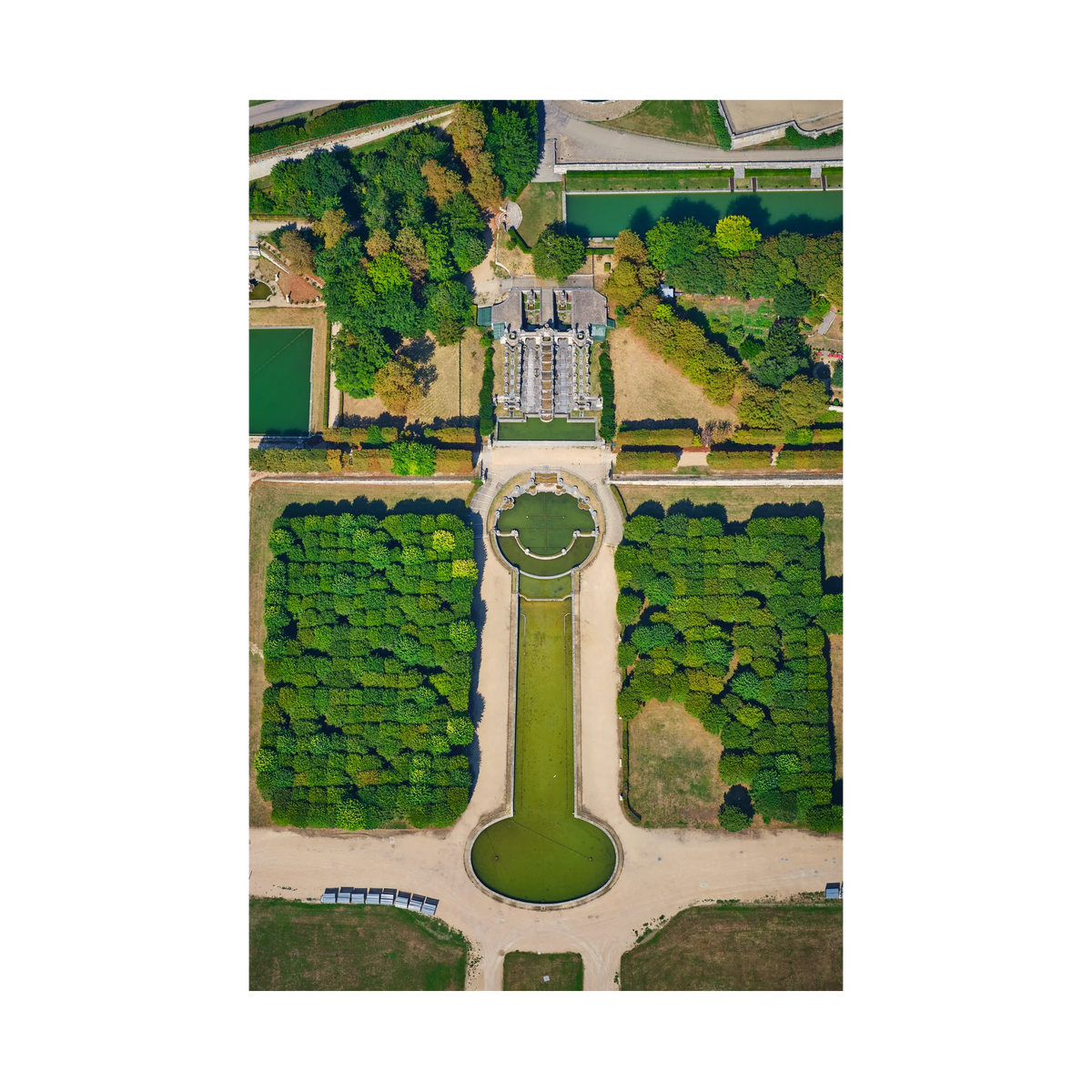 Overhead view of formal gardens in the Paris region, with green pools, pale paths, rows of trees and an ornate cascade; print only
