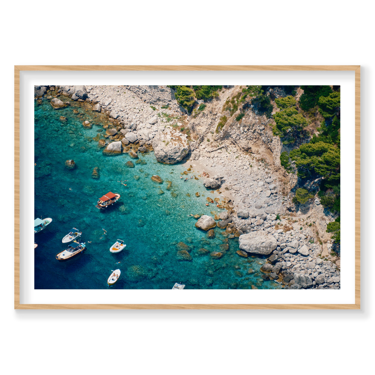 Swimmers and small boats in clear turquoise water beside the pale rocky shore of Capri, Italy, natural timber frame.