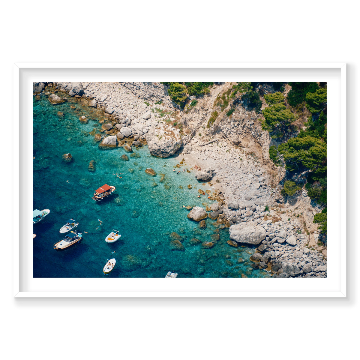 Swimmers and small boats in clear turquoise water beside the pale rocky shore of Capri, Italy, white frame.