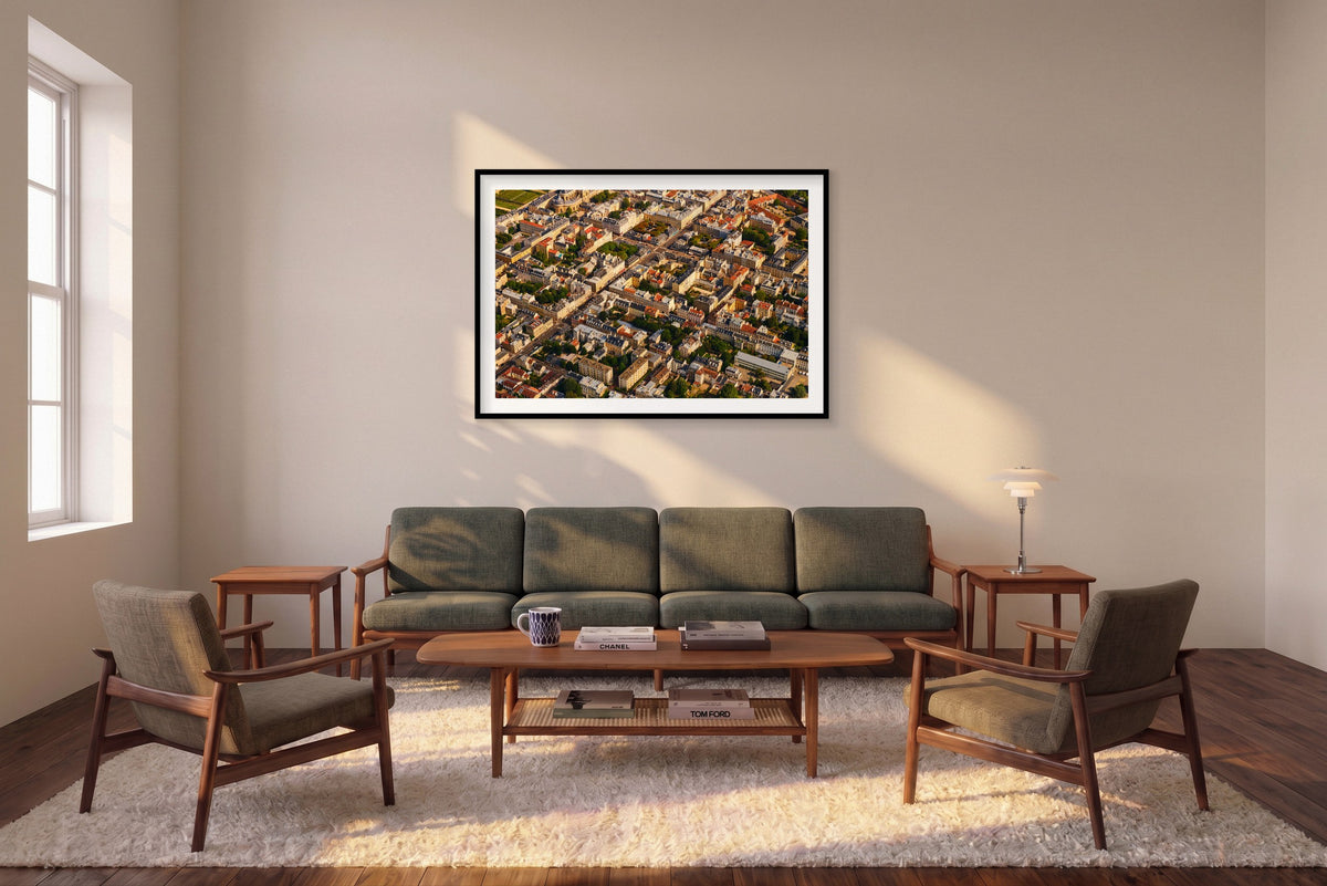 Aerial view of pale buildings, grey and red rooftops, courtyards and tree-lined streets in the Paris region, France; black framed print in a room setting