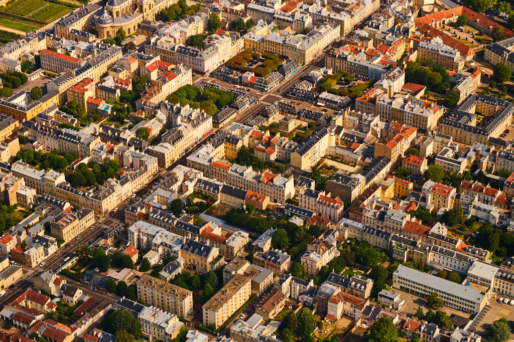 Aerial view of pale buildings, grey and red rooftops, courtyards and tree-lined streets in the Paris region, France; print only