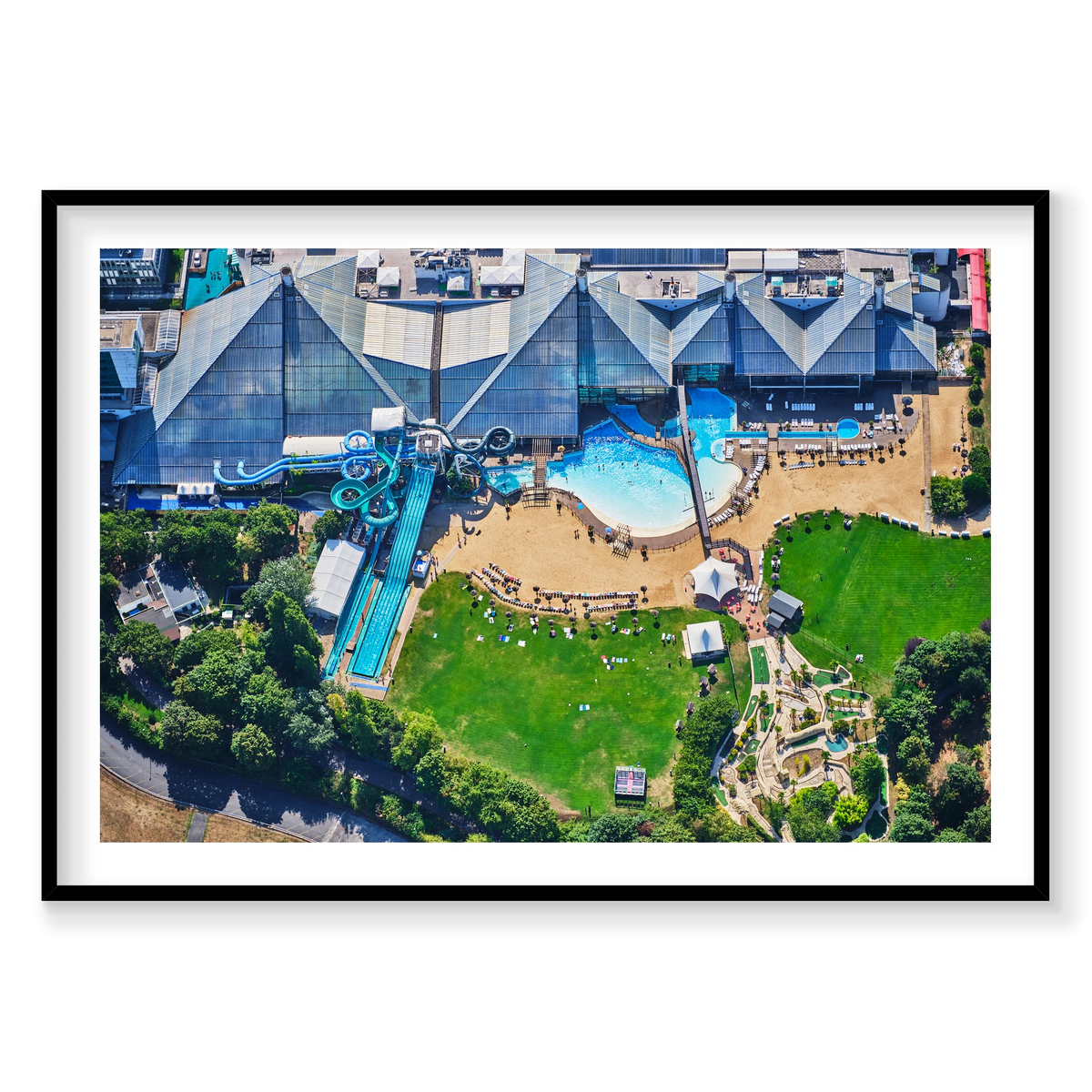 Aerial view of a water park in the Paris area, with blue slides, swimming pools, sun loungers and green lawns; black frame