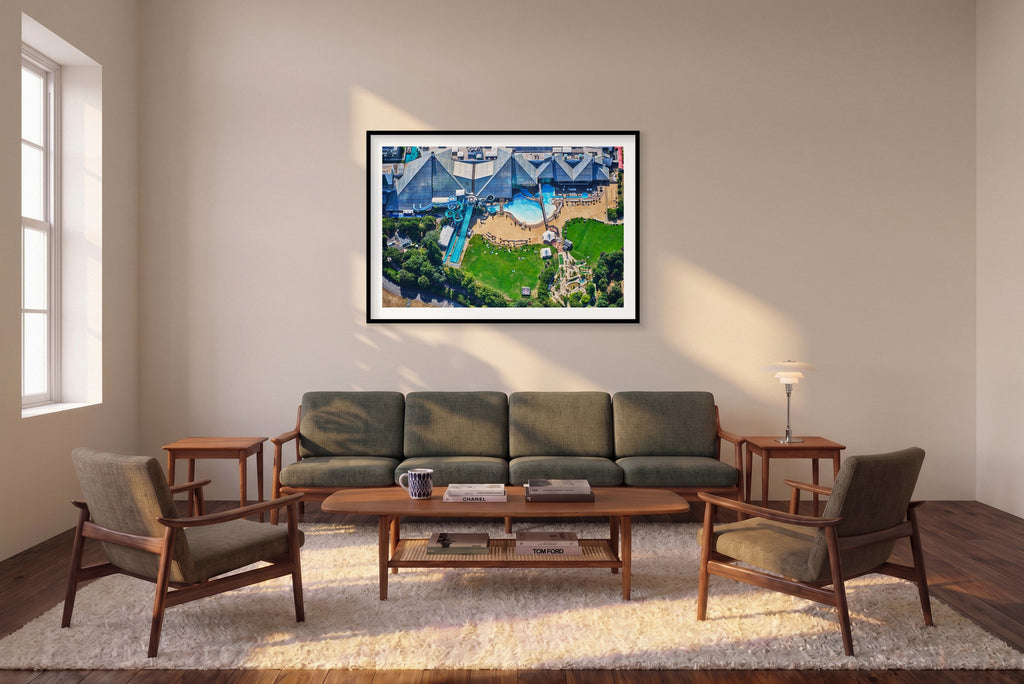 Aerial view of a water park in the Paris area, with blue slides, swimming pools, sun loungers and green lawns; black framed print in a room setting