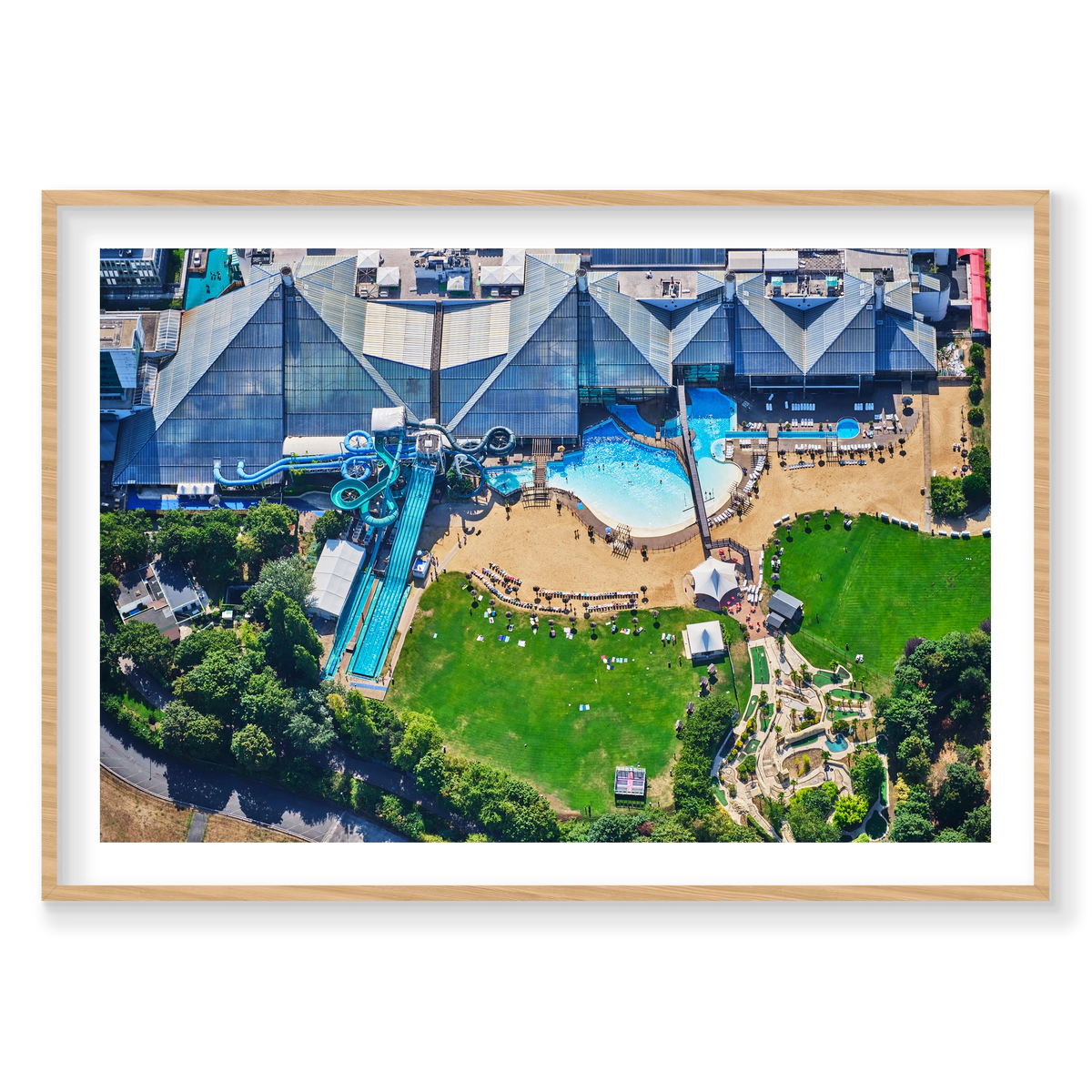 Aerial view of a water park in the Paris area, with blue slides, swimming pools, sun loungers and green lawns; natural timber frame