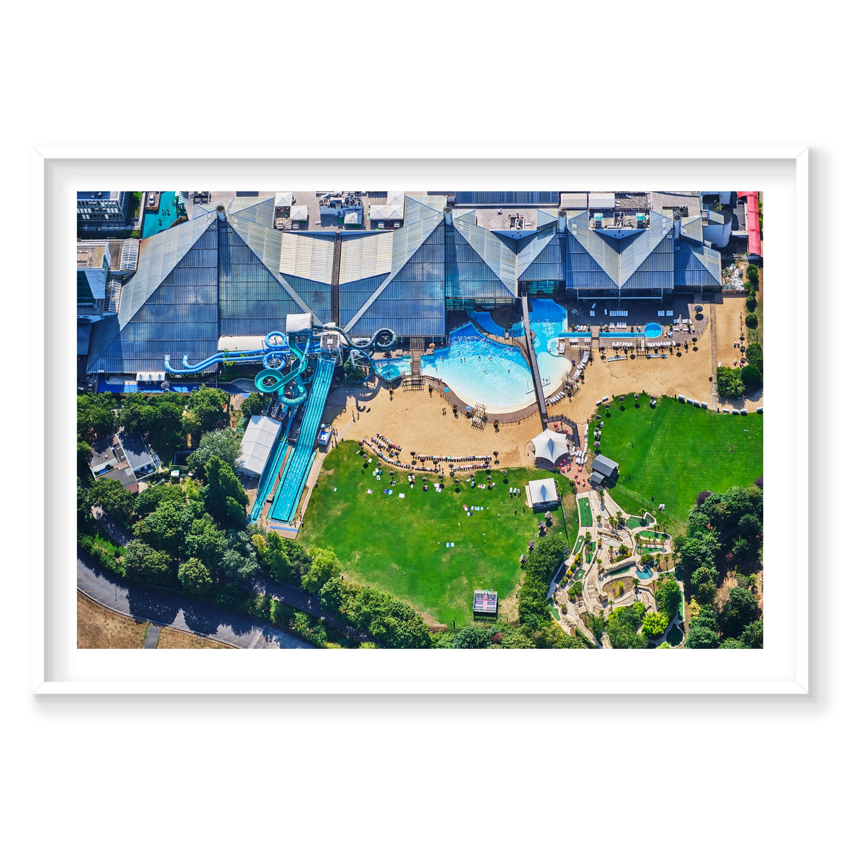 Aerial view of a water park in the Paris area, with blue slides, swimming pools, sun loungers and green lawns; white frame