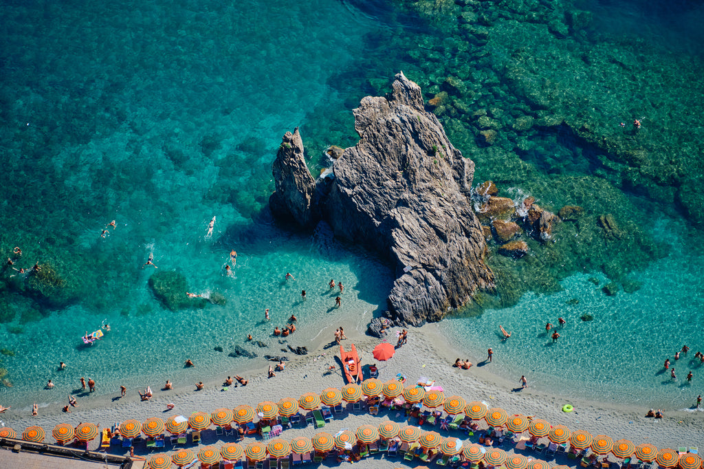 Scoglio di Fegina rock surrounded by swimmers and turquoise water, with orange-striped umbrellas at Monterosso al Mare, Cinque Terre, Italy, print-only presentation.