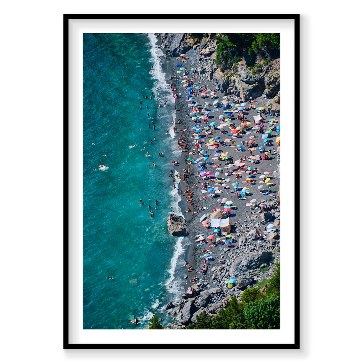 Colourful umbrellas and swimmers along the dark beach beneath rocky cliffs at Punta Corvo, Montemarcello, Italy, black frame.