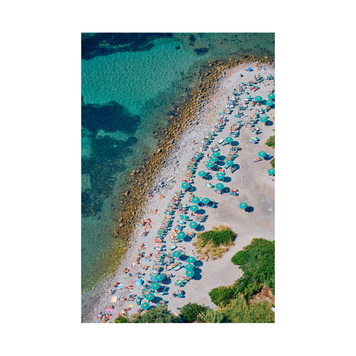 Green umbrellas and sunloungers beside clear water on the pebbled shore of Spiaggia Punta Secco, Palmaria Island, Italy, print-only presentation.