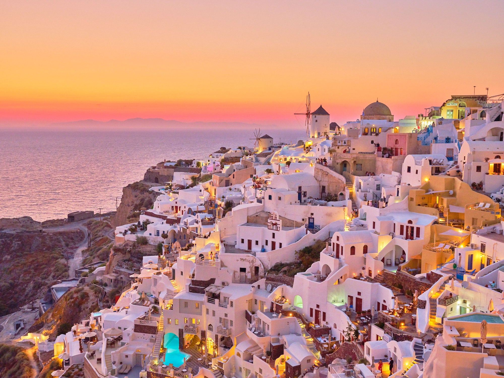 Oia village cliffside at sunset with white-washed buildings and golden lights, Santorini Greece, photography print by Remy...