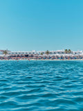 Ornos Beach Greece viewed from turquoise water with white buildings and beach umbrellas, photography print by Remy Gerega