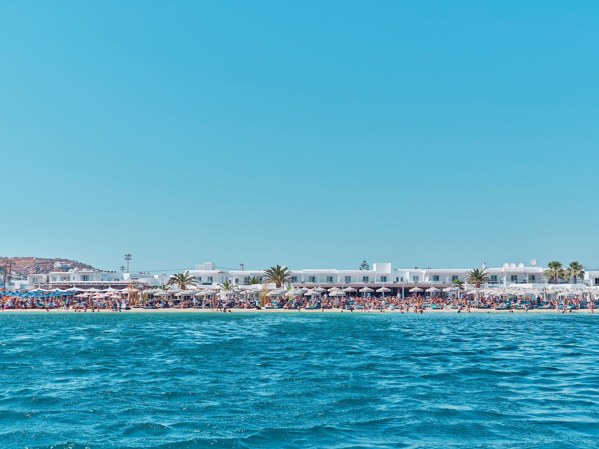 Ornos Beach Mykonos Greece from turquoise waters, white-washed buildings and palm trees, photography print by Remy Gerega